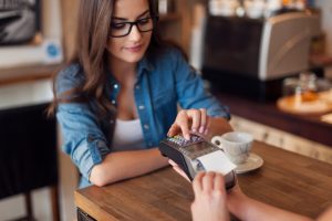 Young woman paying for cafe by credit card reader