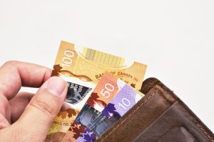 Hand holding one hundred Canadian banknotes (CAD) in brown leather wallet on white background